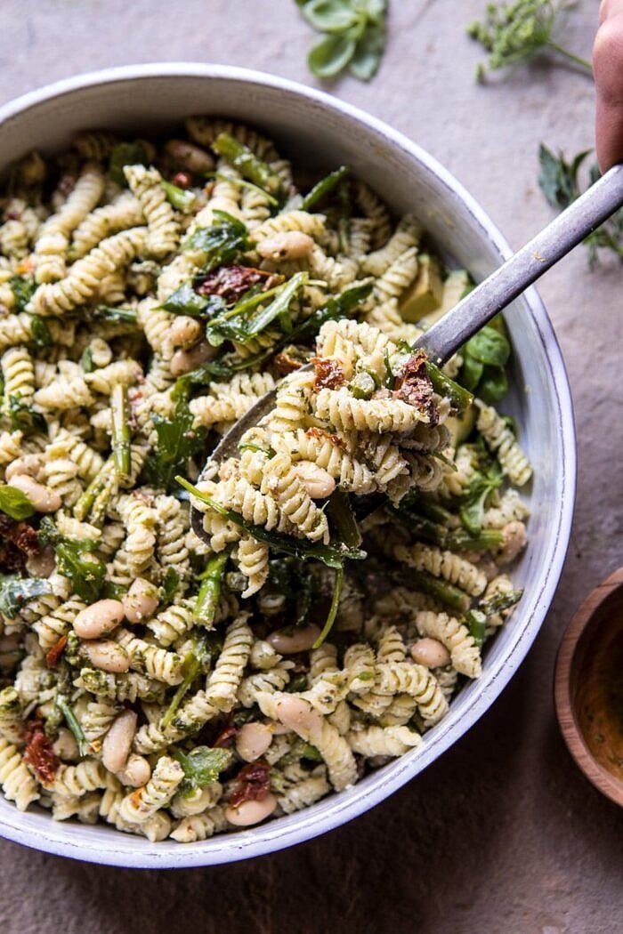 overhead photo of Sun-Dried Tomato, White Bean, and Goat Cheese Pasta Salad with spoonful of pasta being removed