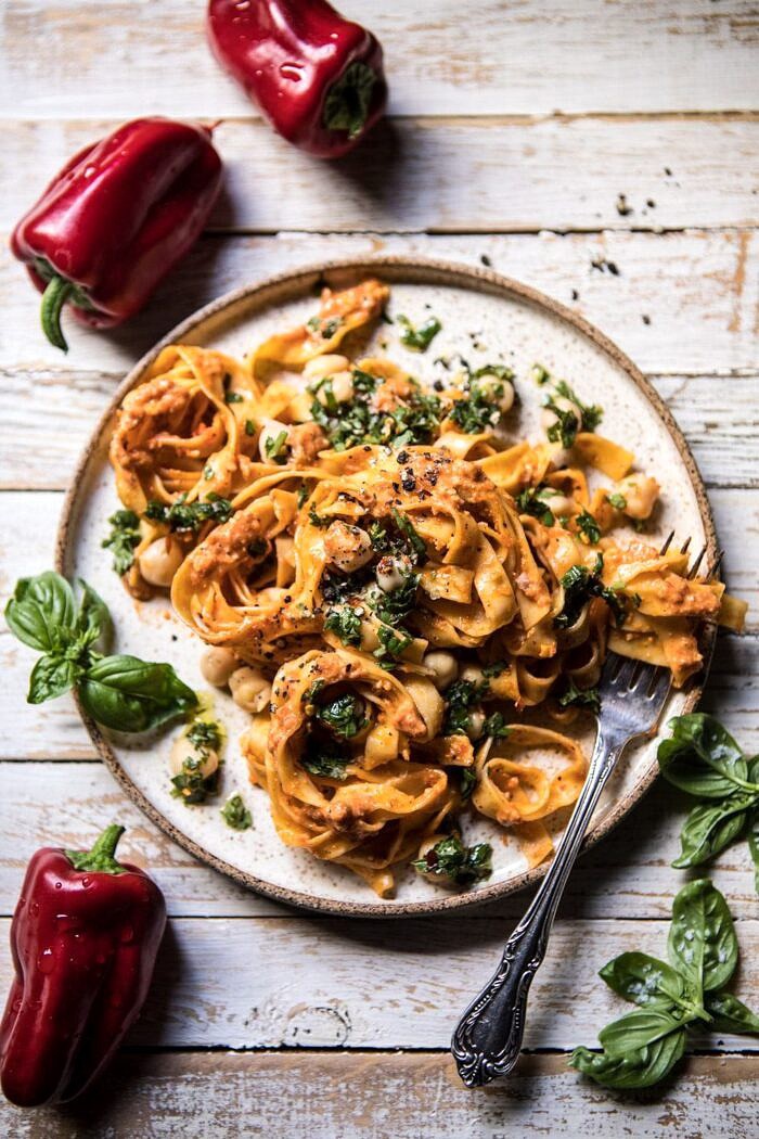 overhead photo of Roasted Red Pepper Pasta with White Beans and Basil with raw peppers and basil next to plate