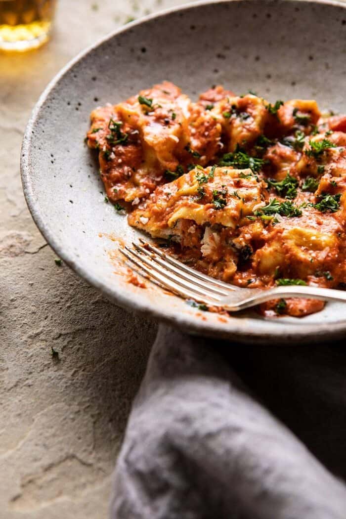 Brown Butter Lobster Ravioli with Tomato Cream Sauce | halfbakedharvest.com #ravioli #Italian #lobster #pastarecipes #pasta #valentinesday side angle close up photo of Brown Butter Lobster Ravioli with Tomato Cream Sauce with bite take out of ravioli
