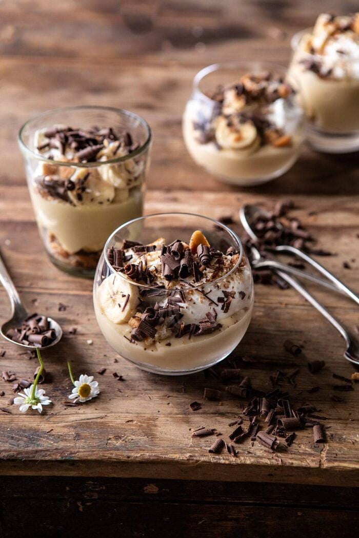 Coconut Banana Cream Pie Parfaits | halfbakedharvest.com #coconutpie #banana #dessertrecipes #easter side angled photo of Coconut Banana Cream Pie Parfaits with spoons on table and 4 parfaits in photo