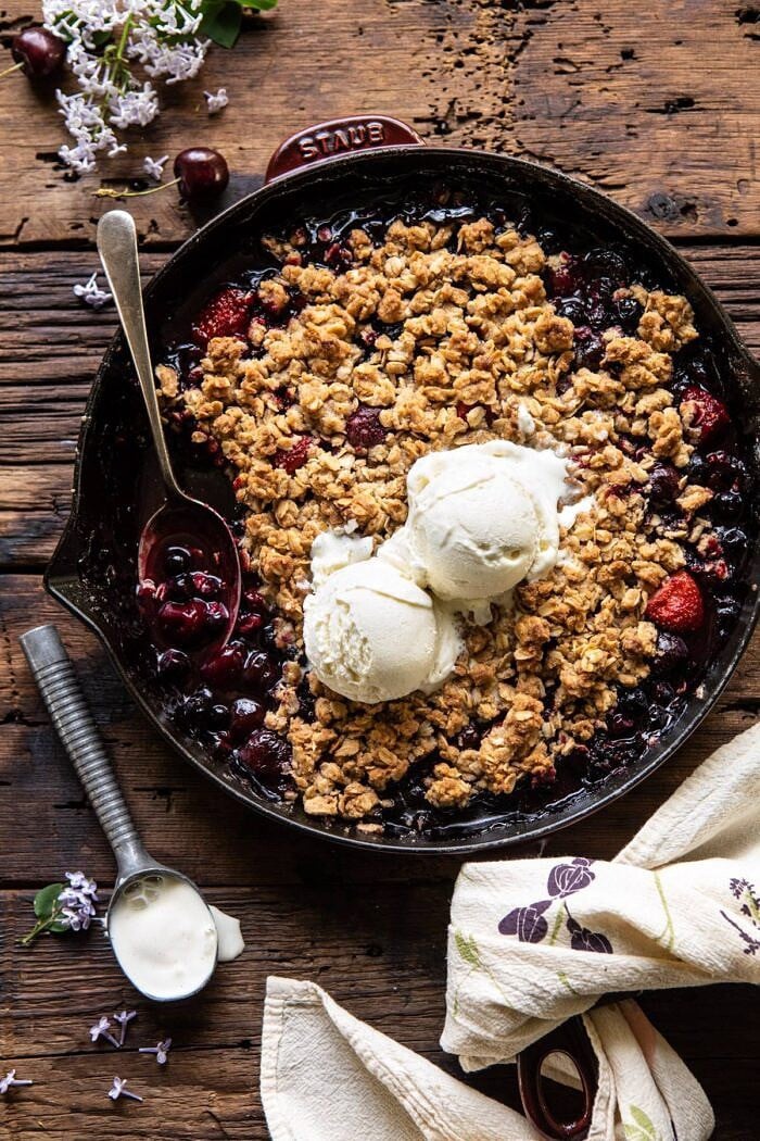 Buttery Cherry Berry Skillet Crisp | halfbakedharvest.com #berries #summerrecipes #easyrecipes #cherries overhead photo of Buttery Cherry Berry Skillet Crisp with ice cream on crisp and spoon in skillet