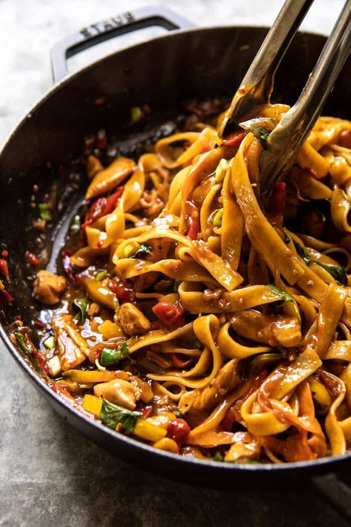 Better Than Takeout Thai Drunken Noodles | halfbakedharvest.com #takeout #noodles #weeknightrecipe #Thai side angle photo of Better Than Takeout Thai Drunken Noodles in cooking pot with tongs pulling the noodles out of the pot