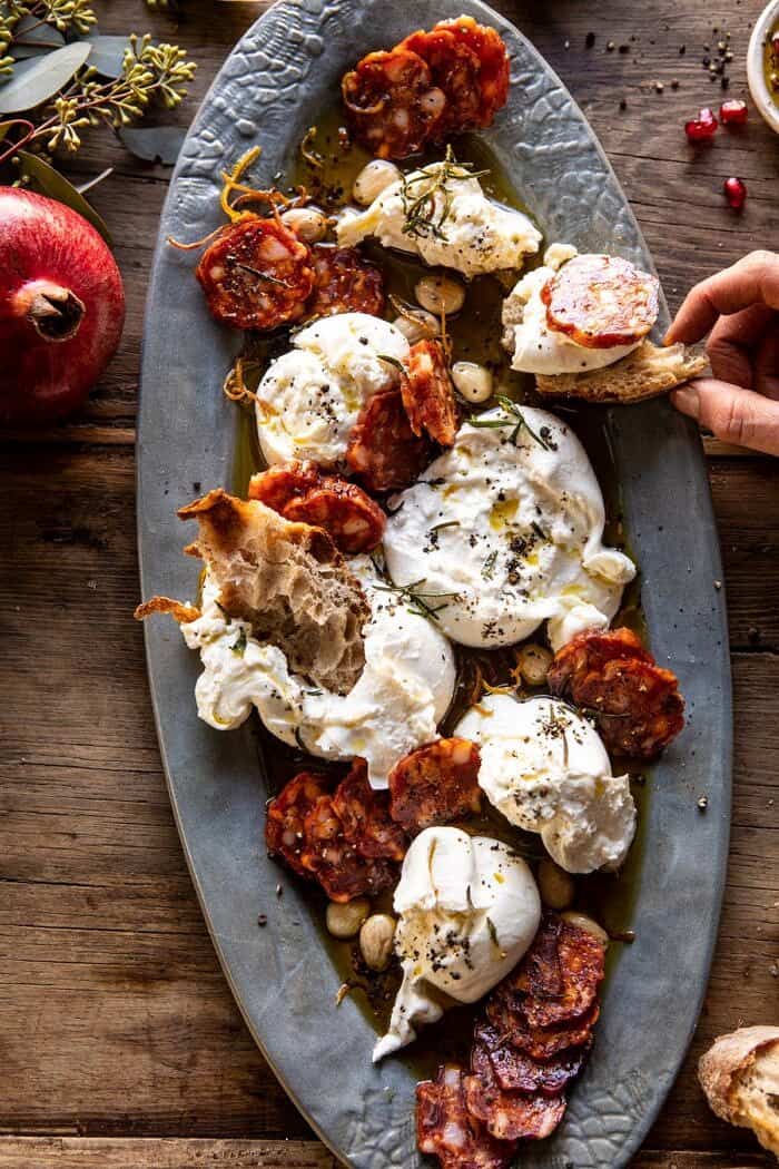 Burrata with Lemon Pepper Salami Bites | halfbakedharvest.com #burrata #appetizer #christmas overhead photo of Burrata with Lemon Pepper Salami Bites and hand taking some of the cheese off the platter