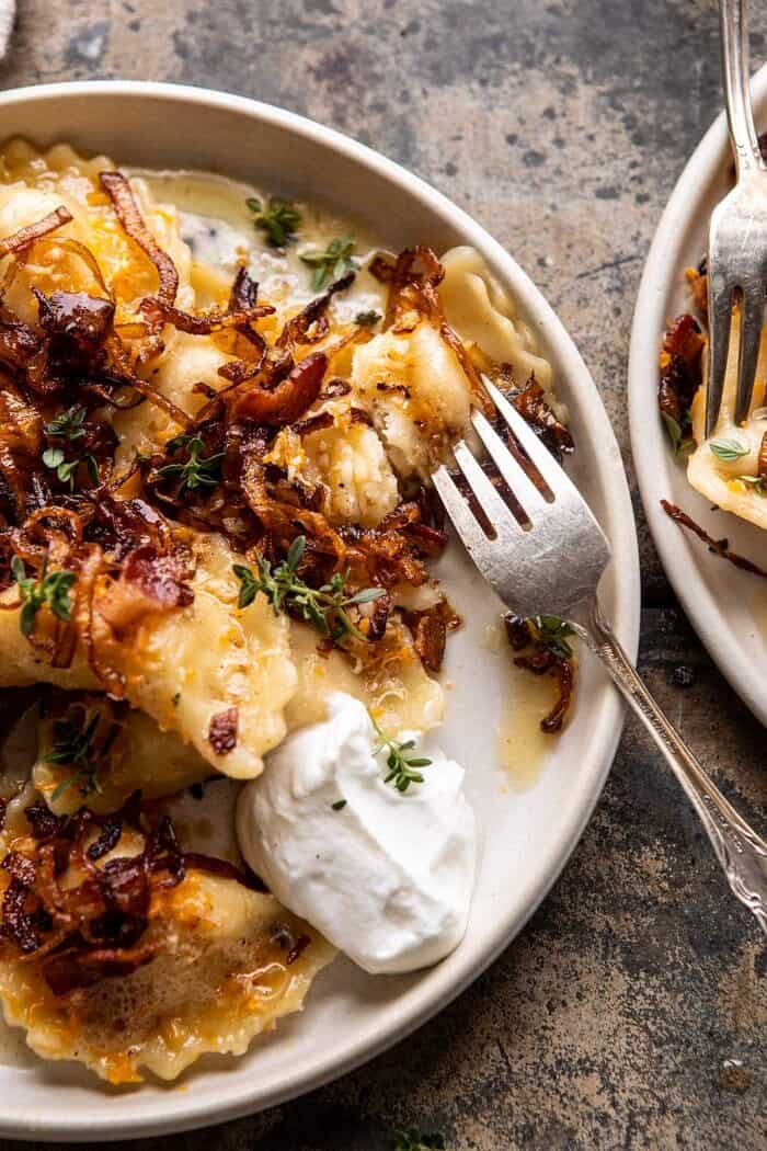 Cheddar Pierogies with Caramelized Onions and Bacon | halfbakedharvest.com #pierogi #homemade #Christmas overhead close up photo of Cheddar Pierogies with Caramelized Onions and Bacon with fork in pierogi