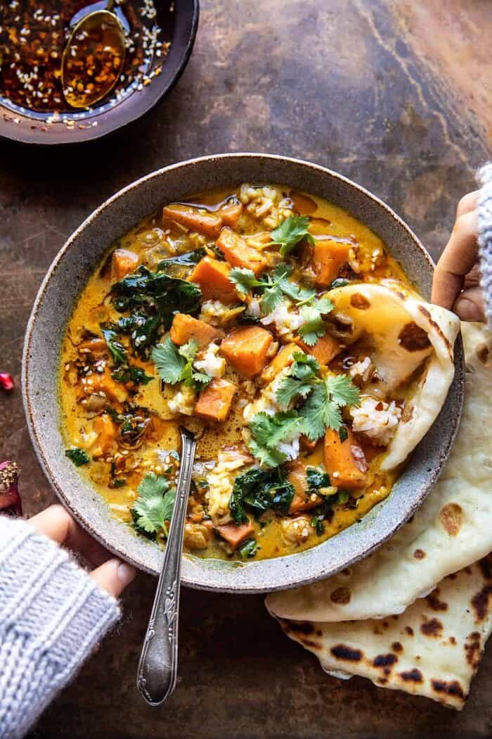 overhead photo of Gingery Coconut Sweet Potato and Rice Stew with Chili Oil with hands on bowl 