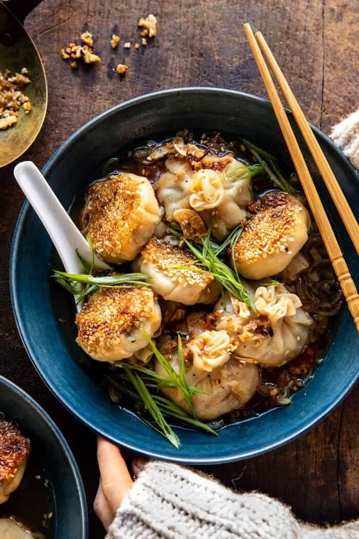 Sesame Chicken Dumplings in Spicy Broth with Garlic Crisps | halfbakedharvest.com overhead photo of Sesame Chicken Dumplings in Spicy Broth with Garlic Crisps and hands on bowl